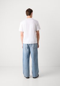 Weißes T-Shirt mit kurzen Ärmeln und lässigen hellblauen Jeans im Relaxed-Fit, die ein klassisches Fünf-Taschen-Design und eine lockere Beinform aufweisen.