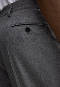 Szare dopasowane spodnie wykonane z teksturowanej tkaniny, z tylną kieszenią zapinaną na czarny guzik oraz kontrastowym ściegiem. Skoncentrowany na minimalistycznym designie.