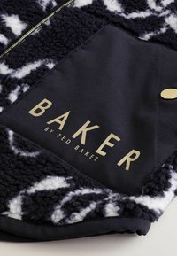 Fleecowy materiał w czarno-białe wzory z złotym logo "BAKER by TED BAKER". Posiada zamek błyskawiczny oraz gładką, granatową kieszeń ze złotym guzikiem.
