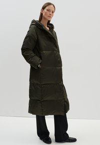 Lange, puffy jas in donkergroen met een capuchon. Bevat grote, gequiltte secties, een ritssluiting en zijzakken.