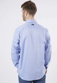 Chemise à manches longues bleu clair avec un motif à pois subtil, col boutonné et étiquette à l'arrière. Matière en coton, coupe décontractée.