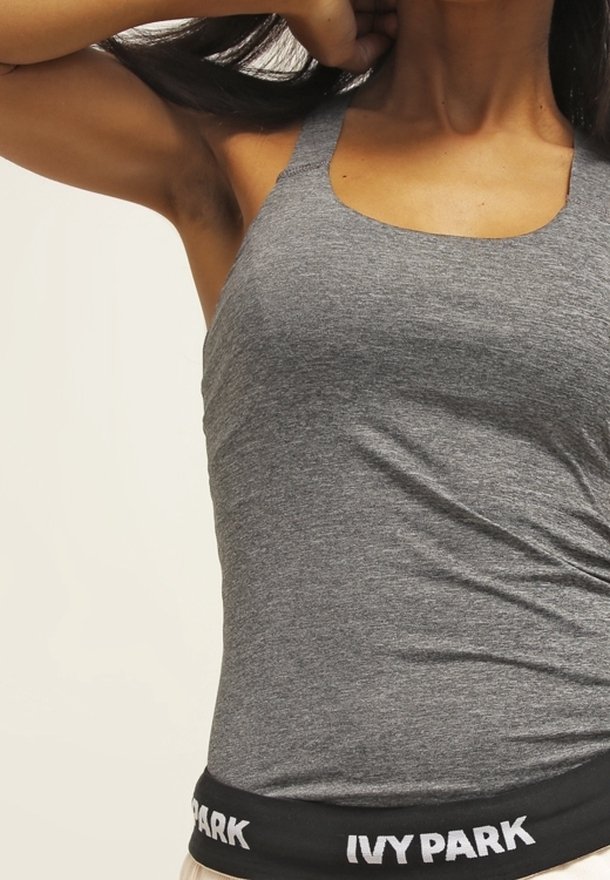 Grå ärmlös topp med en åtsittande design, tillverkad av mjukt tyg. Har ett svart midjeband med "IVY PARK" i vit text.