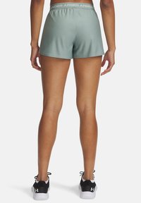 Šviesiai žali sportiniai šortai su prigludusia forma ir elastinga juosta, ant kurios yra „Under Armour“ logotipas. Dėvimi su juodais sportiniais bateliais.