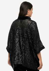 Poncho negro de lentejuelas con cuello de terciopelo, que presenta un corte holgado, mangas anchas y una superficie texturizada acentuada por brillantes lentejuelas.