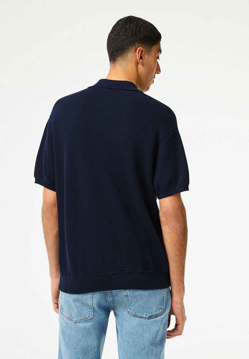 Polo-shirt bleu marine à manches courtes en tissu texturé, doté d'un col classique et d'une coupe décontractée, associé à un jean en denim bleu clair.