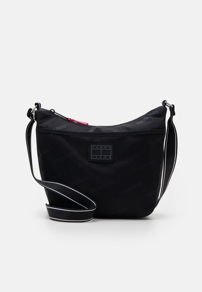 Sac à épaule noir Tommy Jeans avec poche avant en mesh, sangle réglable avec surpiqûres blanches et tirette de fermeture éclair rose.