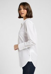 Witte button-up blouse van een gladde, lichte stof. Kenmerkt zich door lange mouwen, een gebogen zoom en een ontspannen pasvorm. Opvallende gele knopen.