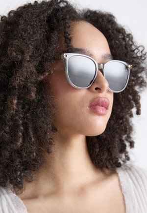 Lunettes de soleil rondes avec des montures en métal argenté et des verres miroités, ornées d'accents dorés sur les branches et d'une finition texturée.
