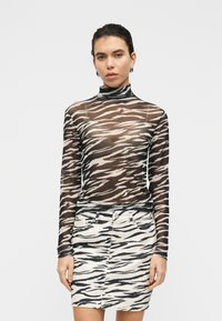 Διαφανές τοπ με ψηλό λαιμό και μακριά μανίκια σε ασπρόμαυρο σχέδιο ζέβρας, συνδυασμένο με τζιν φούστα μολύβι με το ίδιο σχέδιο ζέβρας και στενή γραμμή.