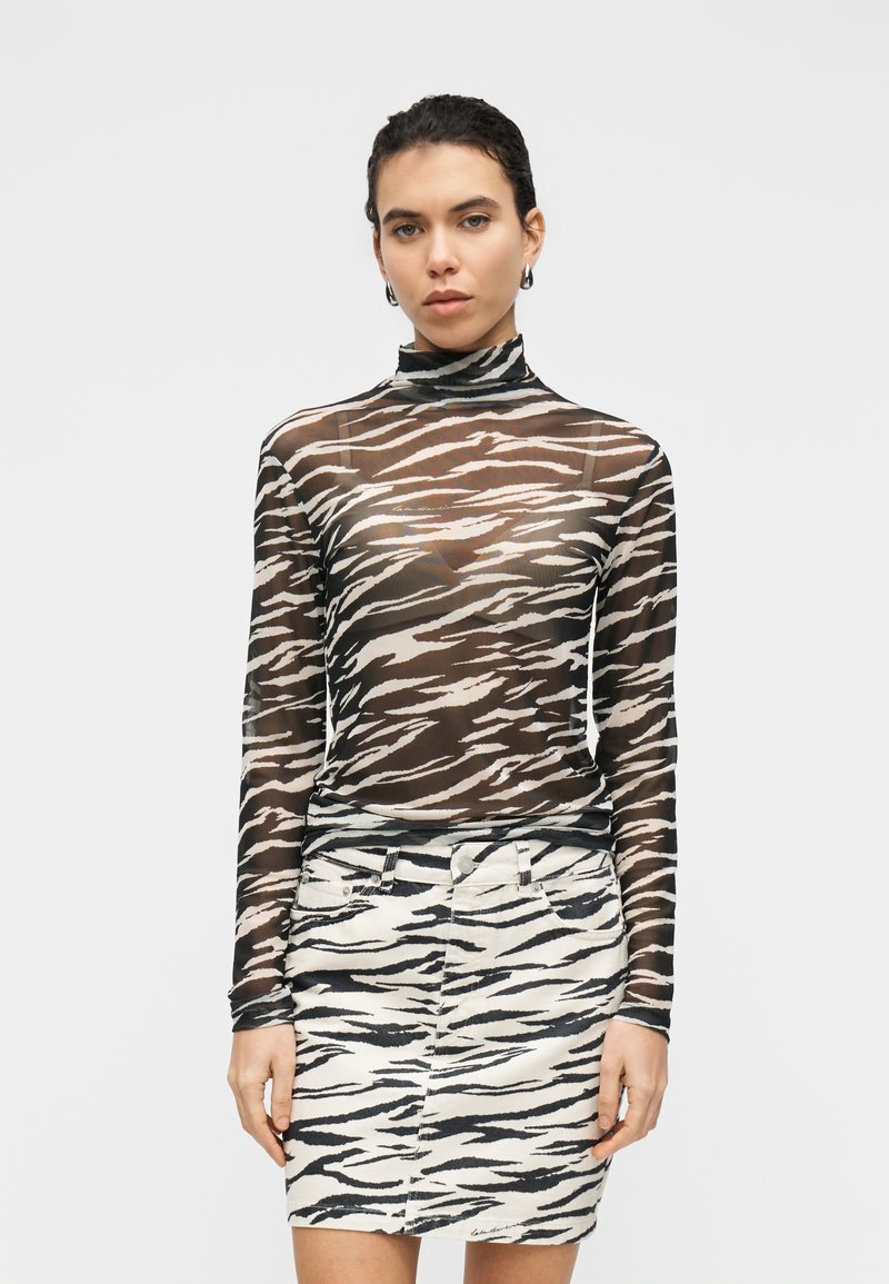 Διαφανές τοπ με ψηλό λαιμό και μακριά μανίκια σε ασπρόμαυρο σχέδιο ζέβρας, συνδυασμένο με τζιν φούστα μολύβι με το ίδιο σχέδιο ζέβρας και στενή γραμμή.