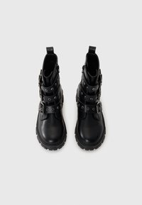 Čierne kožené členkové topánky s viacerými popruhmi a cvočkami, s masívnou podrážkou a bočným zipsom pre jednoduché obúvanie.