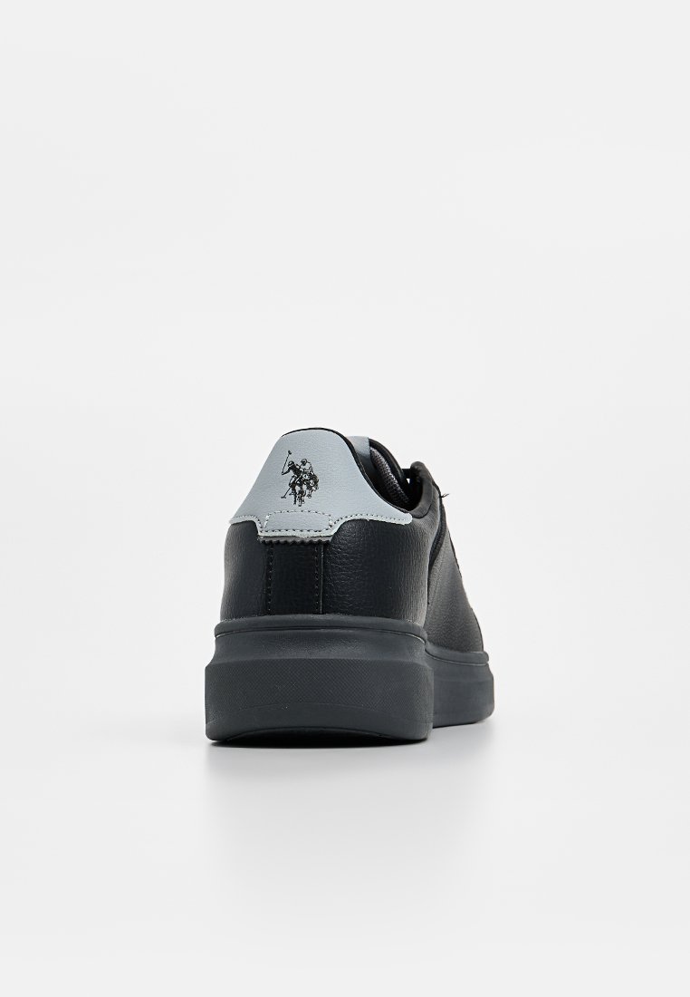Zapatilla de cuero negra con un talón en gris, que presenta un logo y una superficie texturizada, puntera redondeada y una suela de goma resistente.