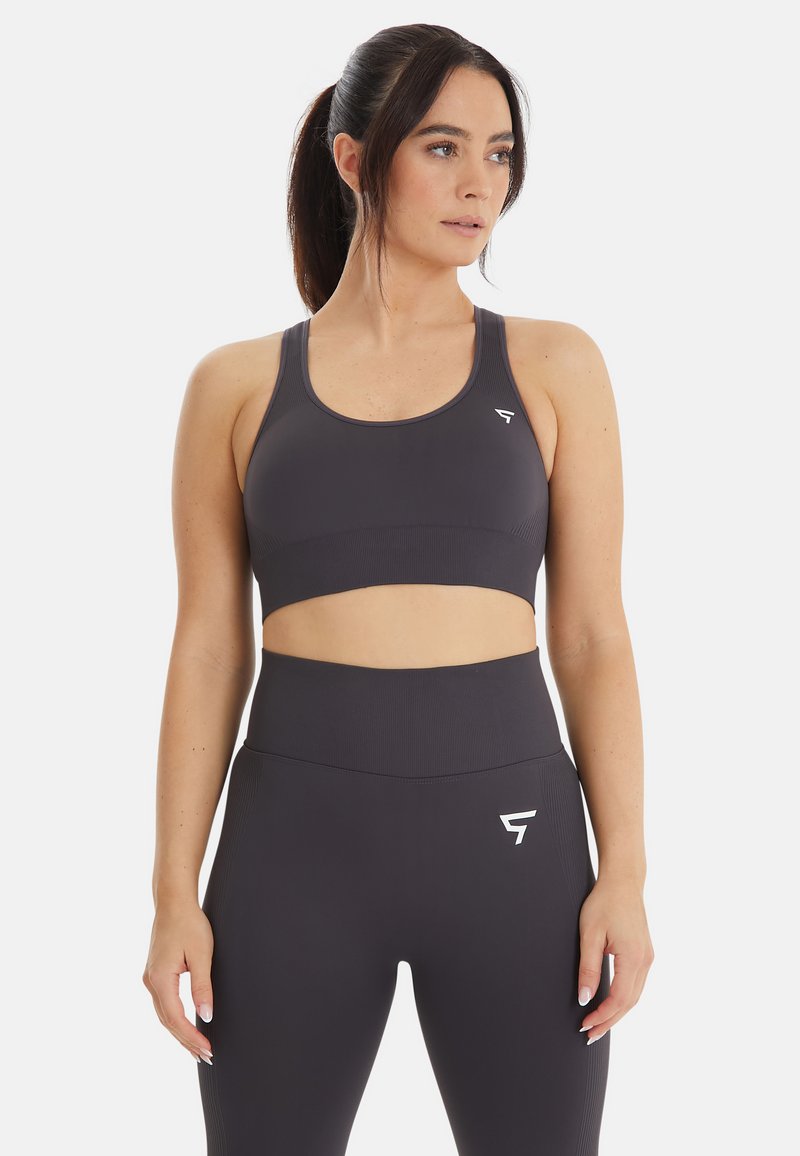 Donkergrijze sportbeha met een geribbelde structuur, een brede onderband en een logo aan de linkerkant. Gecombineerd met bijpassende hoge taille leggings.