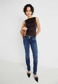 Top sin mangas negro, jeans de mezclilla azul y tacones negros de punta. El top tiene una textura suave, mientras que los jeans presentan un ligero desgastado.