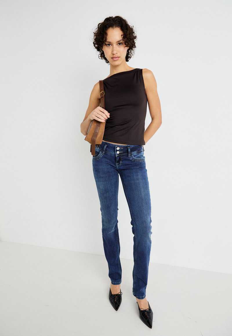 Schwarzes ärmelloses Top, blaue Denim-Jeans und schwarze spitze Absätze. Das Top hat eine glatte Textur, während die Jeans eine leichte Ausbleichung aufweisen.