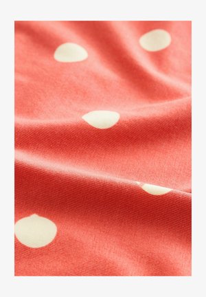 Tissu corail à pois blancs, avec une texture douce et une surface légèrement côtelée, drapée pour montrer sa fluidité et son motif.