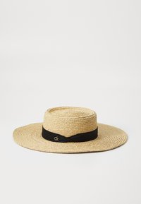 Stråhatt med bred brem og flat topp, med et svart satengbånd og en liten logoaccent. Naturlig tekstur og lys beige farge.