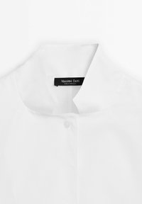 Camicia di cotone bianca con colletto alla coreana, dotata di una chiusura a un pulsante e un'etichetta che recita "Massimo Dutti, Made in Portugal."