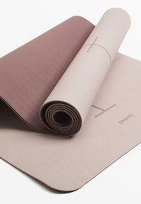 Yogamat met een gestructureerd oppervlak, gedeeltelijk opgerold; heeft een lichtroze kleur met een donkere bordeaux accent. Duurzaam materiaal.