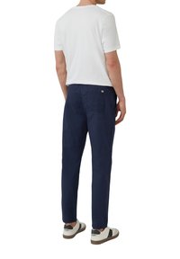 Witte katoenen T-shirt, ontspannen pasvorm, gecombineerd met navyblauwe linnen broek, rechte pijp, zichtbare achterzak en witte sneakers met zwarte accenten.
