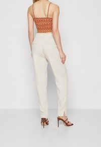 Pantalons ajustés de couleur crème avec une texture lisse. Dotés d'une jambe légèrement fuselée et de fentes à la cheville. Sandales à talons hauts marron.