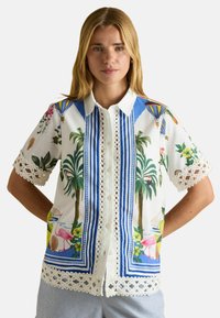 Short-sleeve button-up shirt in white linen with colorful floral and palm tree patterns, blue stripes, and lace accents on the sleeves.
