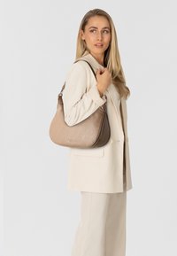 Borsa a tracolla di colore marrone chiaro con un design testurizzato, caratterizzata da una forma curva, chiusura con zip e una tracolla per il trasporto.