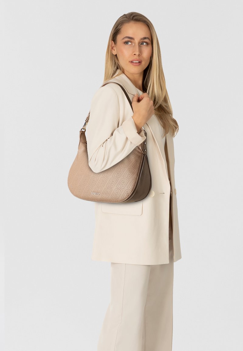 Borsa a tracolla di colore marrone chiaro con un design testurizzato, caratterizzata da una forma curva, chiusura con zip e una tracolla per il trasporto.