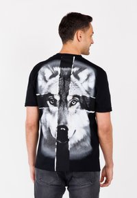 Camiseta negra con un gran gráfico detallado de un lobo en la parte posterior. Mangas cortas, cuello redondo, hecha de algodón y con una textura suave.