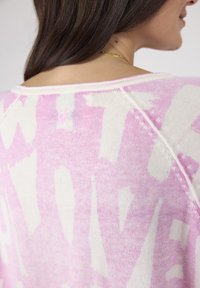 Leichter Strickpullover mit einem pink-weißen abstrakten Muster, einem Rundhalsausschnitt und sichtbaren Nähten entlang der Nähte.