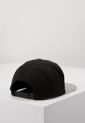 Casquette snapback noire avec sangle réglable et visière plate grise reposant sur une surface blanche sur un fond uni.