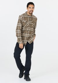 Bruin en tan geblokt flanellen shirt met twee borstzakken, gecombineerd met zwarte broek en zwarte laarzen. Eenvoudig, functioneel ontwerp.