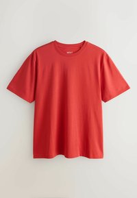 T-shirt rouge uni à manches courtes et col rond, suspendu à plat sur un fond clair, avec une petite étiquette blanche "NEXT" à l'intérieur du col.
