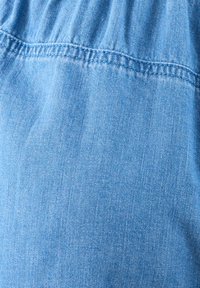 Jasnoniebieska tkanina dżinsowa o gładkiej fakturze i subtelnym, tkanym wzorze. Posiada marszczone szwy na górnej krawędzi.