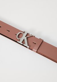 Calvin Klein bőr öv puha rózsaszínben, ezüst színű "CK" logós csattal, több lyukkal az állítható méretezésért.
