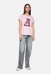 Rosa Baumwoll-T-Shirt mit einem grafischen Aufdruck einer Katze in Schwarz und Pink, kombiniert mit hellgrauen weit geschnittenen Jeans mit weißen Nähten.