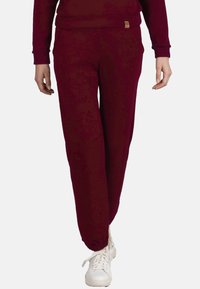 Bordeaux joggerbroek met elastische boorden, zijzakken en een klein merkembleem, gecombineerd met witte sneakers. Glad textuur.