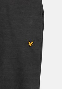Black fabric pants featuring a textured finish and a small yellow eagle logo embroidered on the left side.