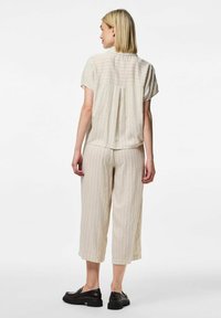 Top beige a righe con maniche corte e pattina quadrata sul retro, abbinato a pantaloni cropped coordinati. Indossato con scarpe con plateau nere.