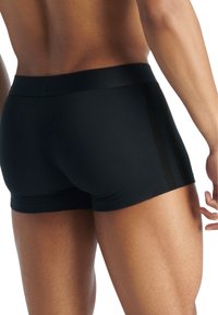 Svarta idrottsshorts med en figurnära design, som har en slät yta och subtila svarta ränder längs sidorna. Midje med medelhög höjd.