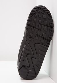 Svart sneaker med texturerad gummisula, framträdande mönstring och Nike-logotyp. Har ett slätt övermaterial med en elegant design.