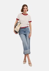 Vit t-shirt med röd vågig kant, blå korta jeans med fransar, beige klackar och en svartvitt väska. Avslappnad outfit.