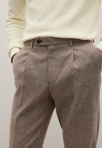 Bruine Herringbone broek met een tailored fit, voorzien van een enkele knoopsluiting en zijzakken, gecombineerd met een crèmekleurige geribbelde trui.