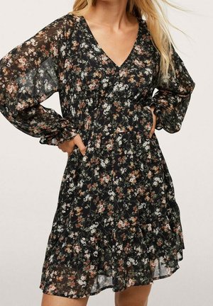 Robe noire à fleurs avec manches longues, décolleté en V profond et ourlet à volants superposés. Confectionnée en tissu transparent orné de motifs floraux multicolores.