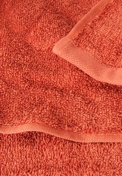 Gros plan d'une serviette en tissu éponge de couleur corail pliée montrant sa texture et ses bords cousus.