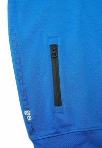 Blå huvtröja med en framficka med dragkedja, svarta dragkedjedetaljer och 'U.S. POLO ASSN.' broderat på sidan i kontrasterande blå.