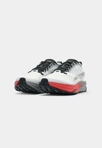 Chaussures de trail running blanches avec des accents rouges, dotées d'une semelle en caoutchouc noir texturé et de lacets noirs, conçues pour la performance et l'adhérence.