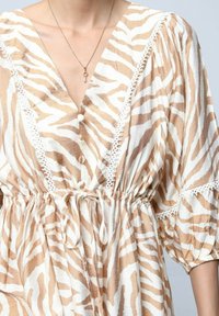 Robe rayée beige et blanche avec une taille cintrée, bordure en dentelle le long des manches et du décolleté, ornée de boutons sur le devant.