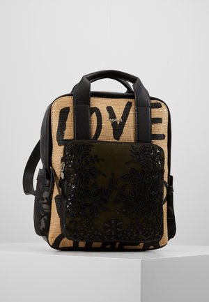 Kwadratowy plecak z czarnymi skórzanymi paskami, przednią częścią z tkaniny w kolorze cielistym z napisem „LOVE” oraz przednią kieszenią ozdobioną czarną kwiatową koronką z zamkiem błyskawicznym.