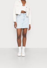 Denim minikjol i ljusblått med fransar, i kombination med en vit kort jacka och vita snörstövlar vid anklarna.